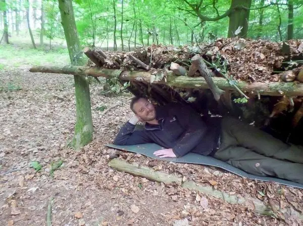 Biwak unter einer selbstgebauten Laubhütte im Wald, auf einer Matte liegend