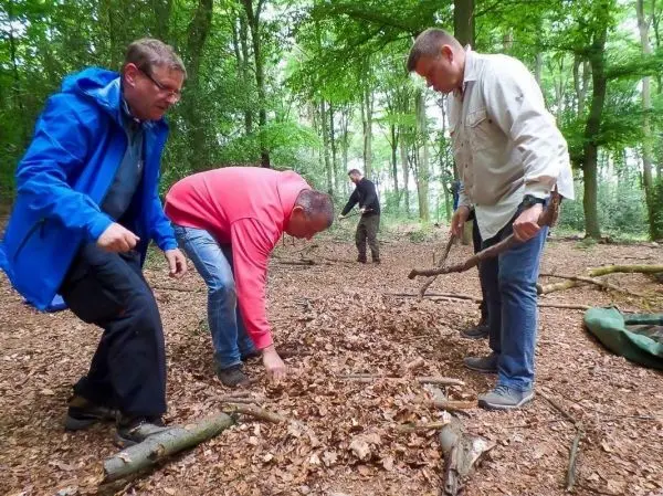 Drei Personen sammeln Äste und Laub im Wald für eine Konstruktion