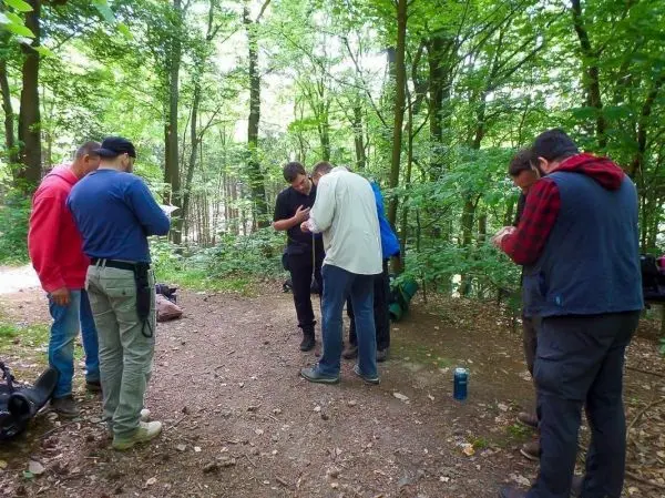 Gruppe betrachtet Kartenmaterial im Wald, Rucksäcke liegen am Boden
