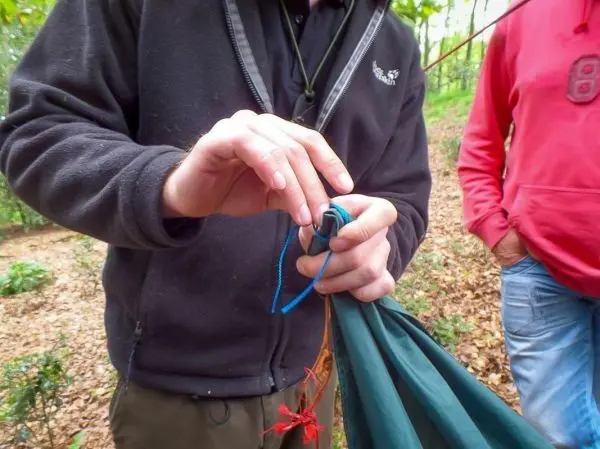 Hände binden eine Schnur an einem Tarp zur Befestigung