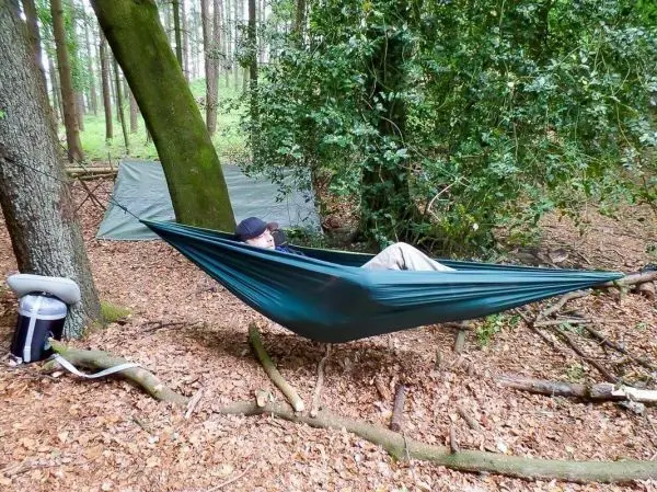 Hängematte zwischen Bäumen mit Person, im Hintergrund Tarp-Notunterkunft