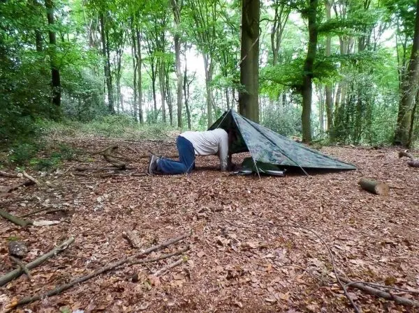 Mann kriecht in eine Tarp-Notunterkunft im Wald