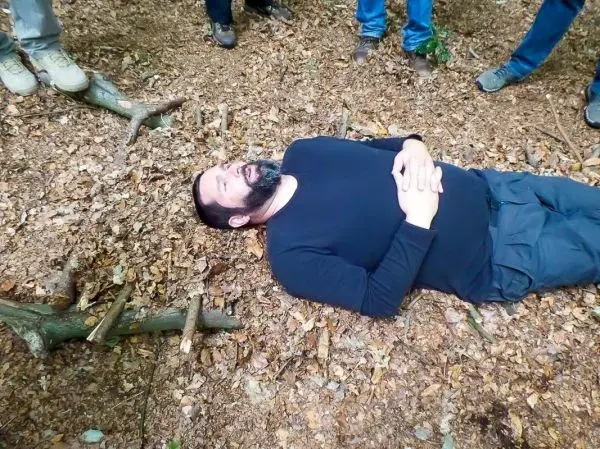 Mann liegt auf dem Boden im Wald, umgeben von Ästen und Laub