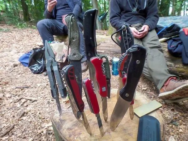 Mehrere Werkzeuge und Messer stehen auf einem Holzscheit im Wald