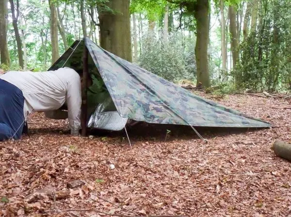 Person kriecht in ein camouflagefarbenes Zelt im Wald beim Überlebenstraining