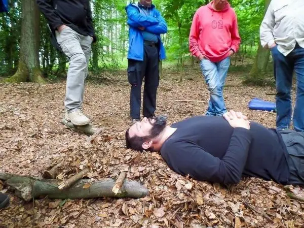 Person liegt auf dem Boden im Wald, umgeben von mehreren stehenden Personen