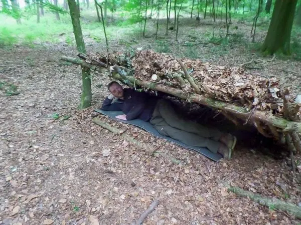 Person liegt unter einer selbstgebauten Laubhütte im Wald