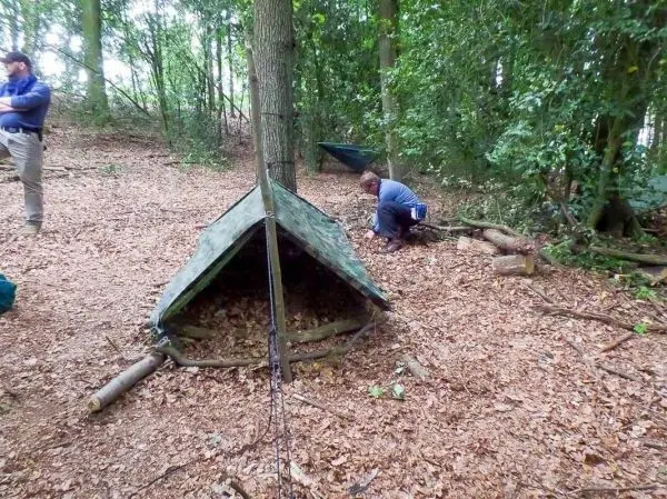 Tarp-Notunterkunft aus Ästen und Plane wird im Wald aufgebaut