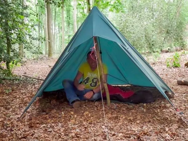 Tarp-Notunterkunft aus einem blauen Tarp, im Inneren sitzt eine Person auf dem Boden