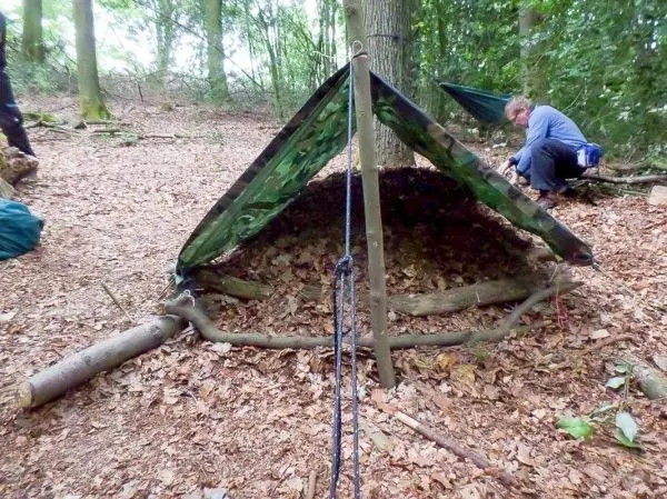 Tarp-Notunterkunft mit Holzgestell und Abspannschnur im Wald aufgebaut