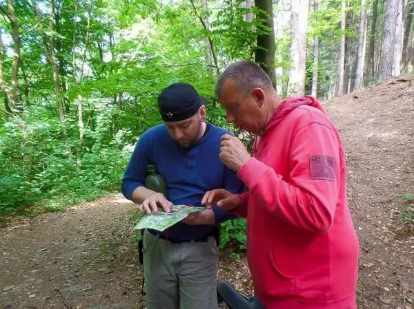 Zwei Personen betrachten eine Karte im Wald und diskutieren die Route