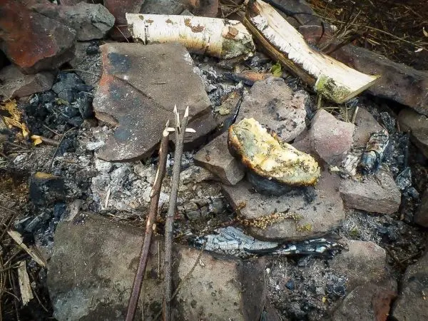 Asche und Steine umgeben von verbranntem Holz und zwei Spießen auf dem Boden