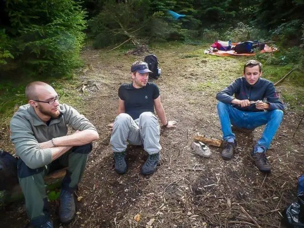 Drei Personen sitzen auf dem Boden in einem Waldgebiet und unterhalten sich