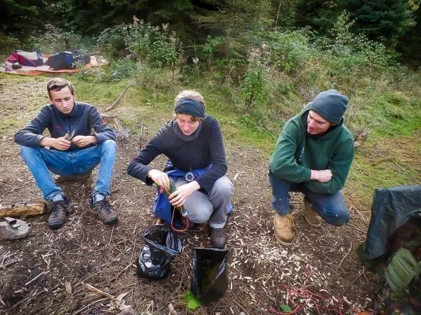 Drei Personen sitzen im Wald und sortieren Ausrüstung in schwarzen Taschen