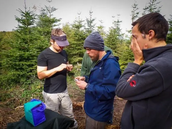 Drei Personen stehen um einen Tisch und betrachten ein Objekt in der Natur