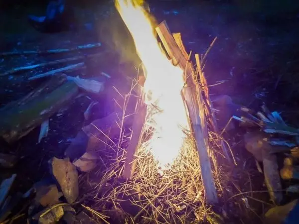 Feuer brennt zwischen Holzstücken und trockenem Gras