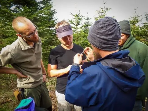 Gruppendiskussion über eine Technik im Wald, Teilnehmer betrachten ein Objekt