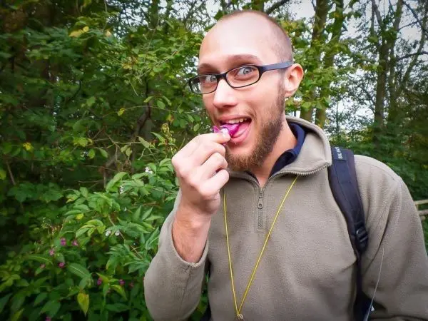 Mann hält eine Blüte vor den Mund und lächelt, im Hintergrund grüne Pflanzen