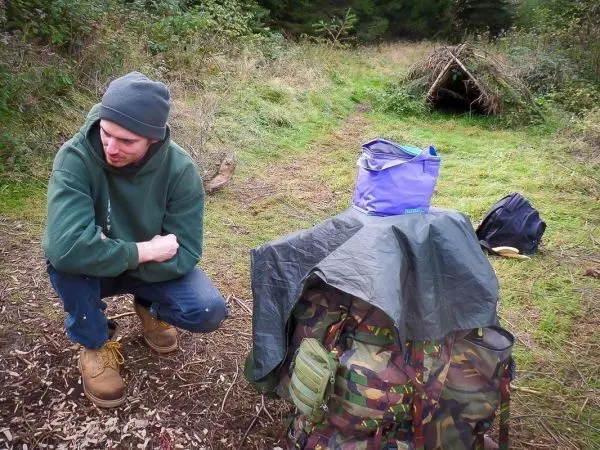 Mann kniet neben einem Rucksack, der mit einer Plane abgedeckt ist