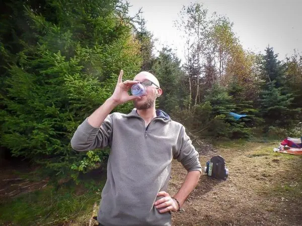 Mann trinkt aus einem Becher in einem Waldgebiet