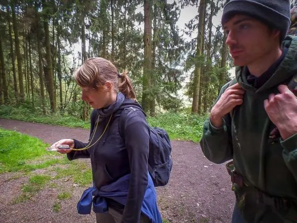 Person betrachtet Karte im Wald, während Begleiter aufmerksam zusieht