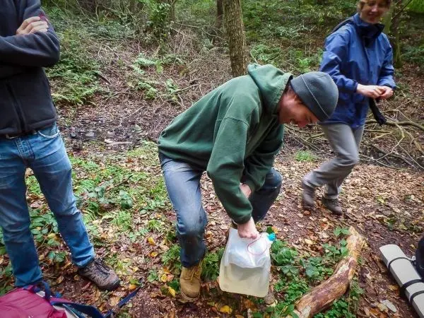Person beugt sich über einen Wasserbehälter im Wald