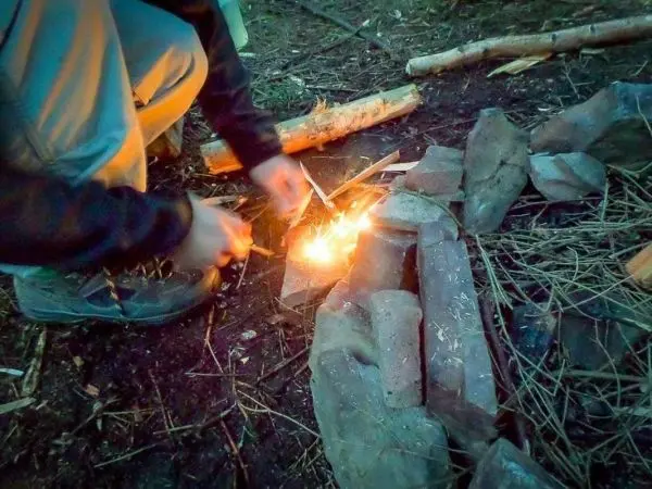 Person entzündet Feuer mit Zündholz im Freien beim Survival Training