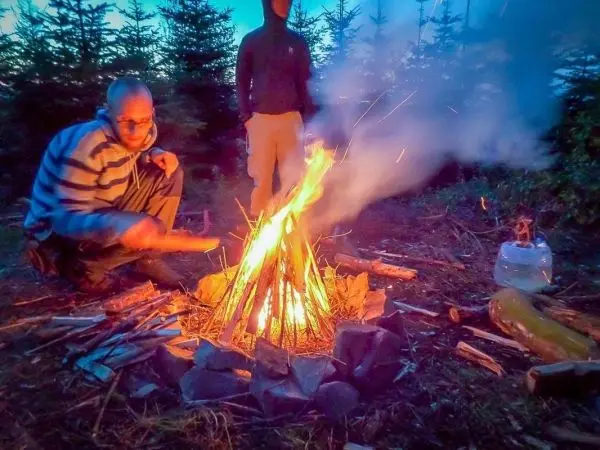 Person fügt Holz zu einem Feuer hinzu im Wald beim Überlebenstraining