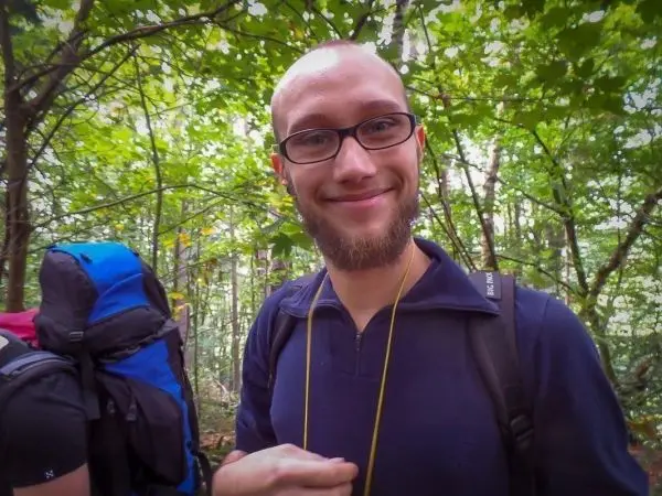 Person lächelt und trägt einen Rucksack im Wald