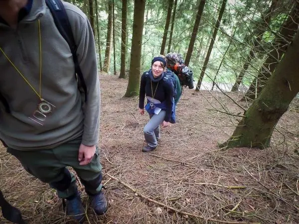 Person wandert mit Rucksack einen steilen Waldhang hinauf