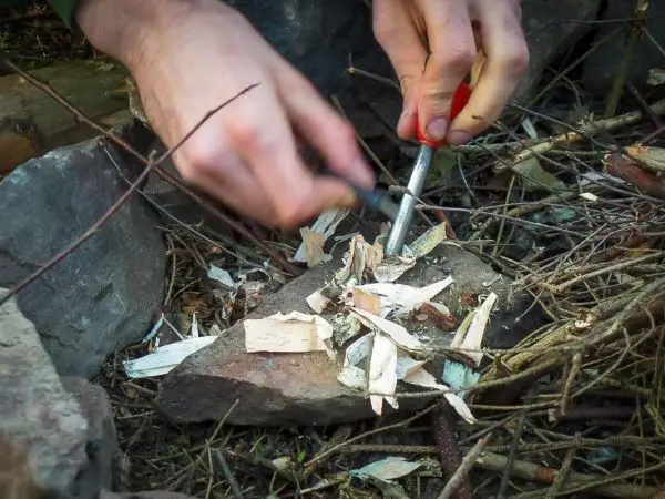 Person zündet Zunder mit Feuerstahl auf einem Stein an beim Survival Training