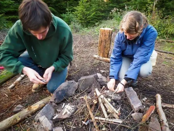 Personen bereiten Feuerstelle mit Holz und Steinen vor beim Survival Training