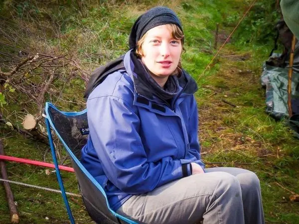 Sitzende Person in blauer Jacke auf einem Campingstuhl in der Natur