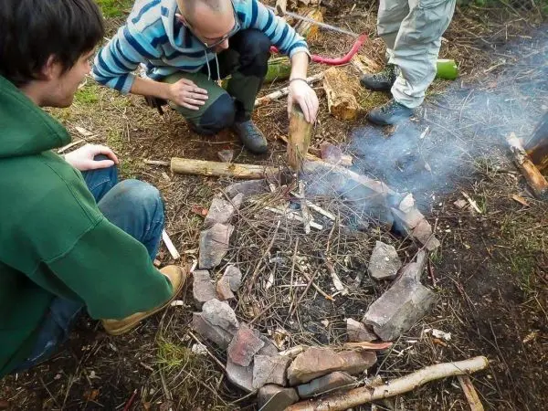 Zunder glimmt in einem Steinkreis, während Holzstücke hinzugefügt werden