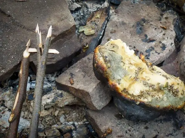 Zunder glimmt neben zwei angespitzten Ästen auf Steinen
