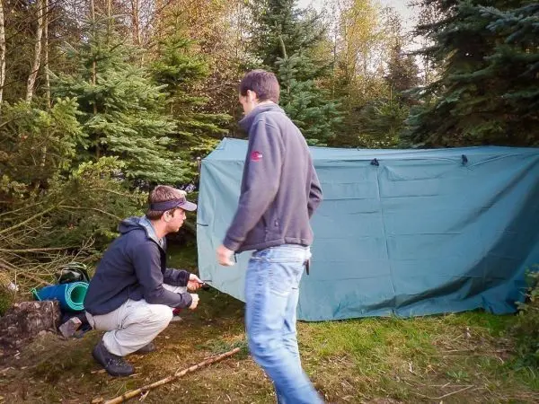 Zwei Personen bauen eine Tarp-Notunterkunft im Wald auf