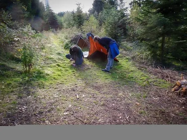 Zwei Personen bauen eine Tarp-Notunterkunft im Wald auf