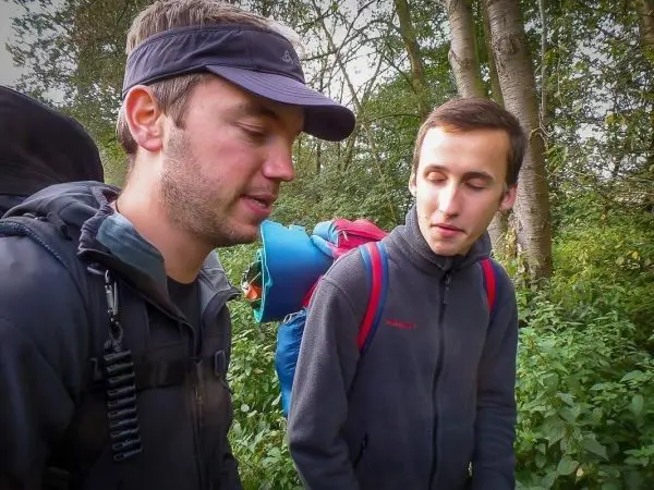 Zwei Personen mit Rucksäcken stehen im Wald und betrachten etwas gemeinsam