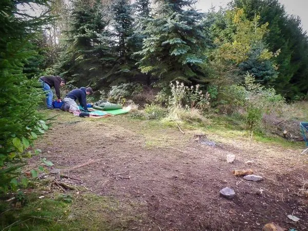 Zwei Personen richten eine Schlafunterlage im Wald her