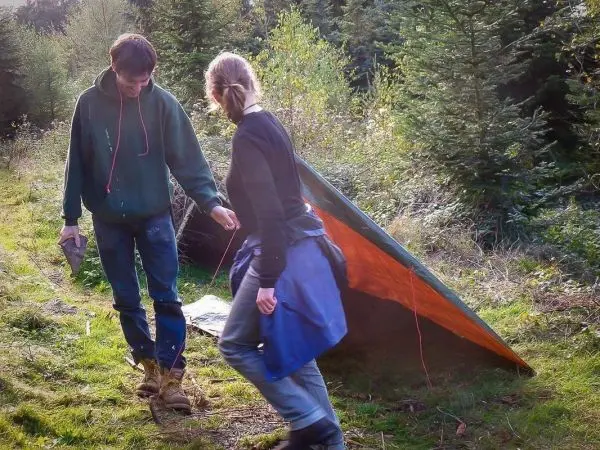 Zwei Personen richten eine Tarp-Notunterkunft im Wald auf