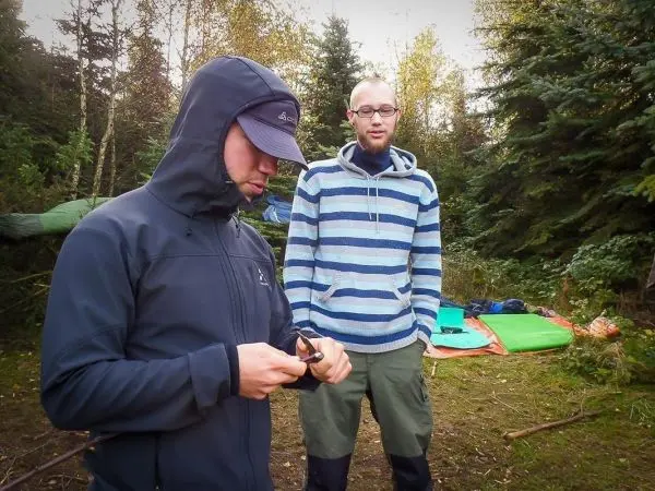 Zwei Personen stehen in einem Waldgebiet, eine Person hält ein Messer in der Hand