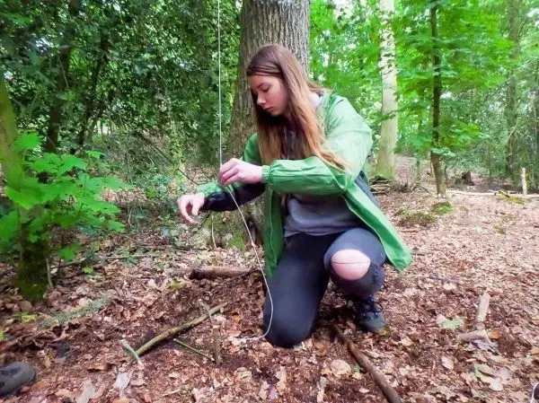 Frau baut eine Schlingenfalle aus Ästen und Schnur im Wald