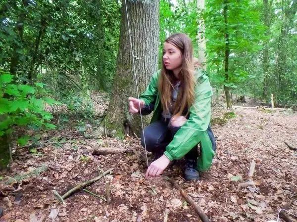 Frau positioniert eine Schnur für eine selbstgebaute Schlagfalle im Wald