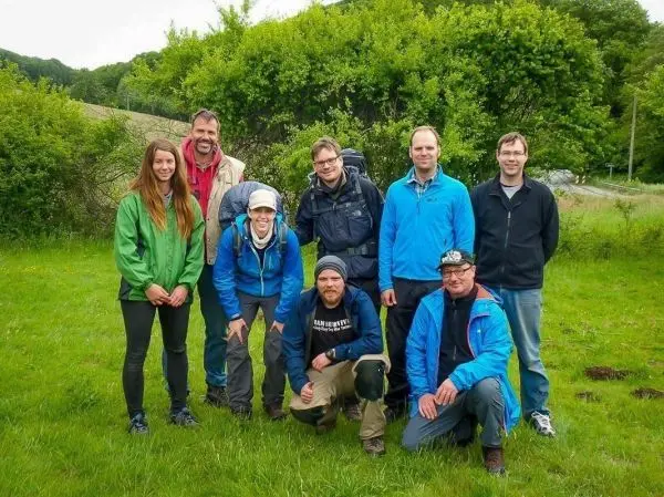 Gruppe von acht Personen in Outdoor-Bekleidung auf einer Wiese