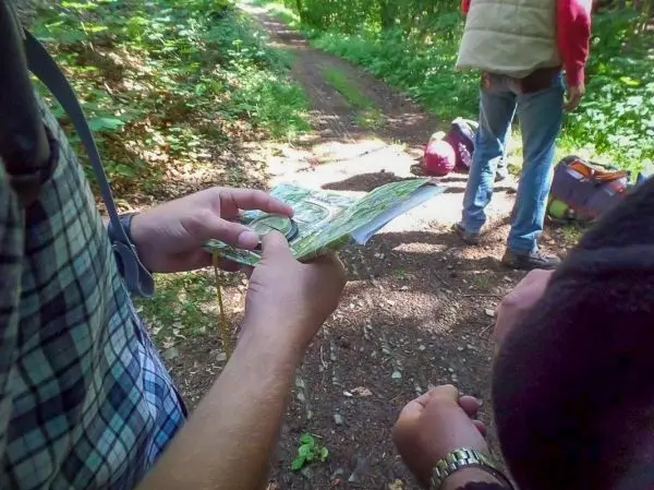 Hände halten eine Karte und einen Kompass auf einem Waldweg