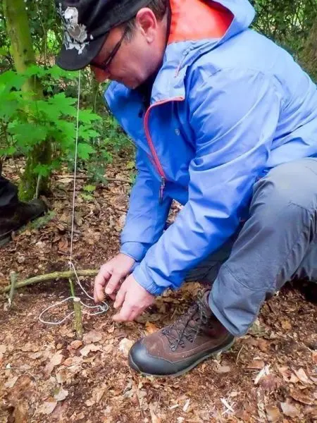 Mann bindet eine Schnur an eine selbstgebaute Schlagfalle im Wald