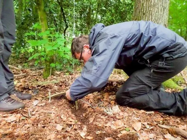 Mann kniet im Wald und richtet eine selbstgebaute Schlagfalle ein