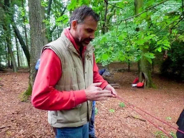 Mann knotet ein Seil unter Bäumen im Wald