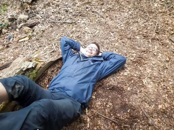 Mann liegt entspannt auf dem Waldboden zwischen Laub und Ästen