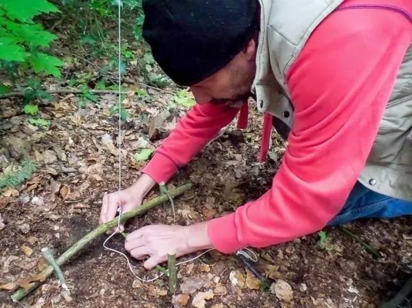 Person baut eine Falle aus Ästen und Schnur im Wald